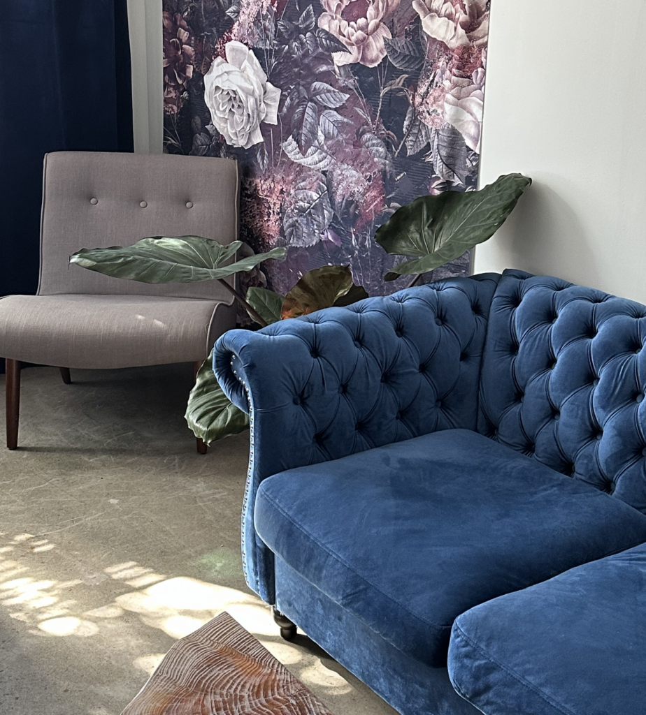 A blue velvet sofa in front of a floral wall.