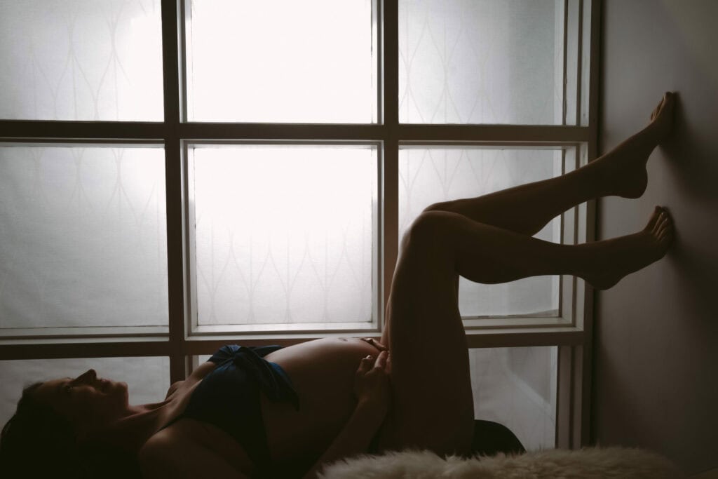 A pregnant woman leaning against a window.