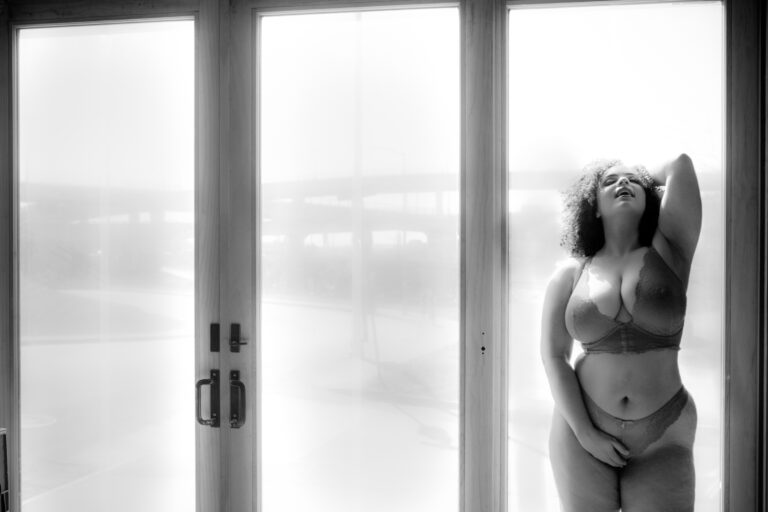 A woman in a lingerie posing in front of a glass door.