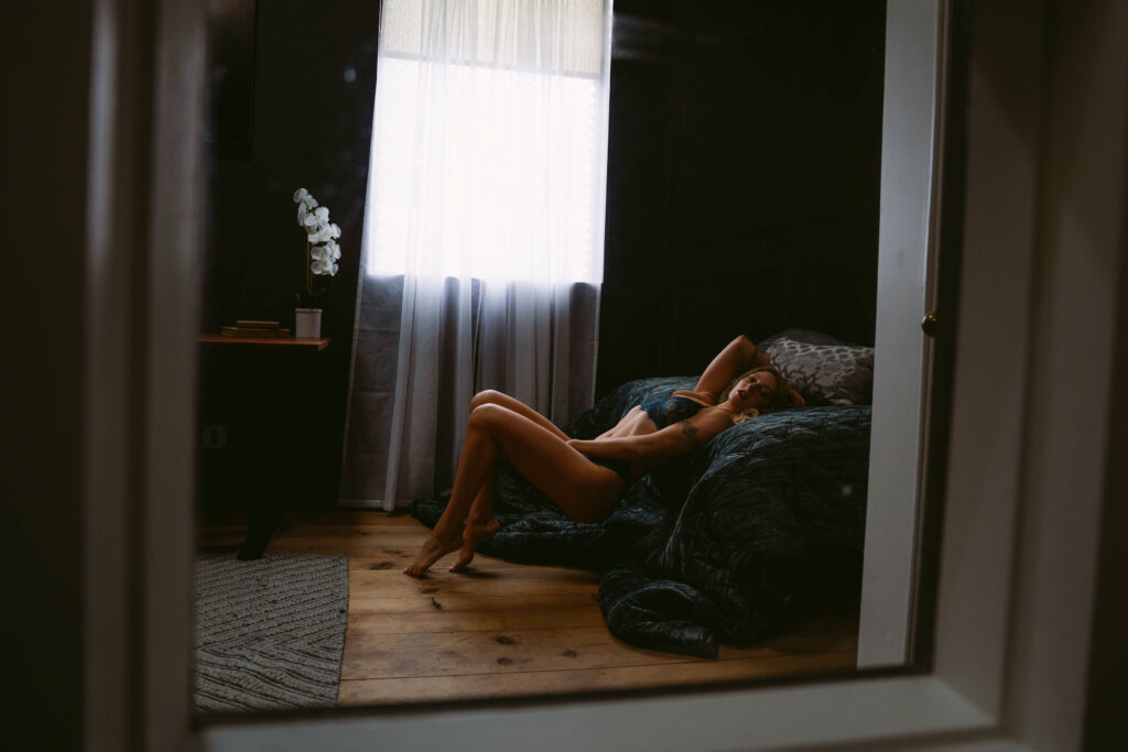 Person relaxing in dim bedroom with sunlight through curtain.