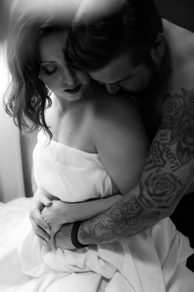 A monochrome photo of a romantic couple embracing, with the focus on their intimate connection and the man's tattooed arms.