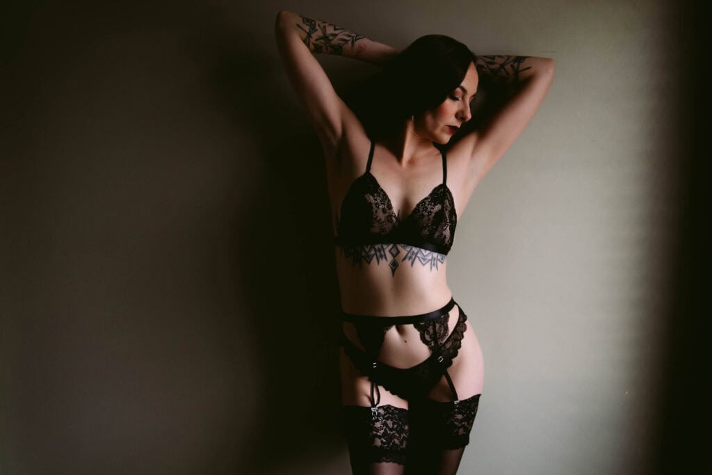 Woman in black lace lingerie with tattoos posing.