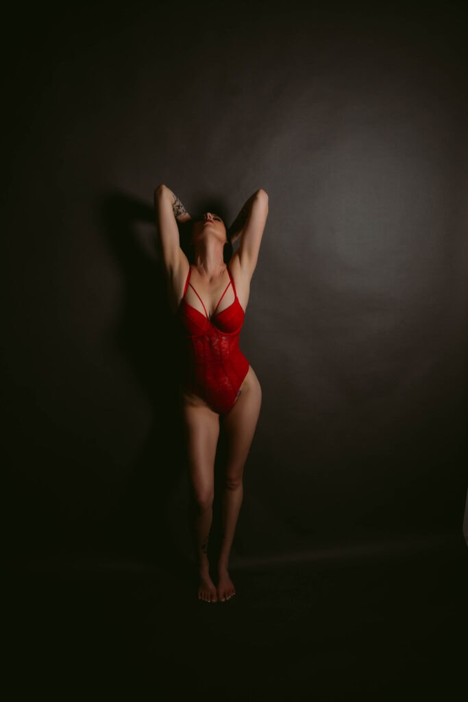 Person posing in red lace lingerie against dark background.