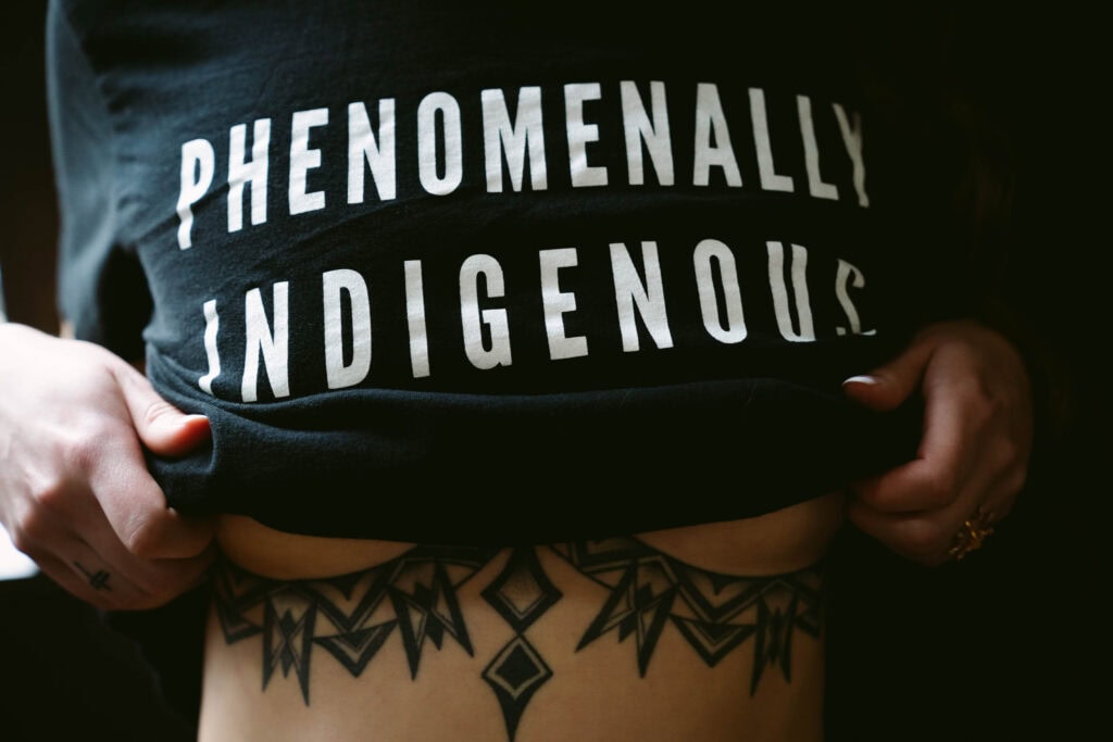 Phenomenally Indigenous shirt with geometric tattoo underneath.