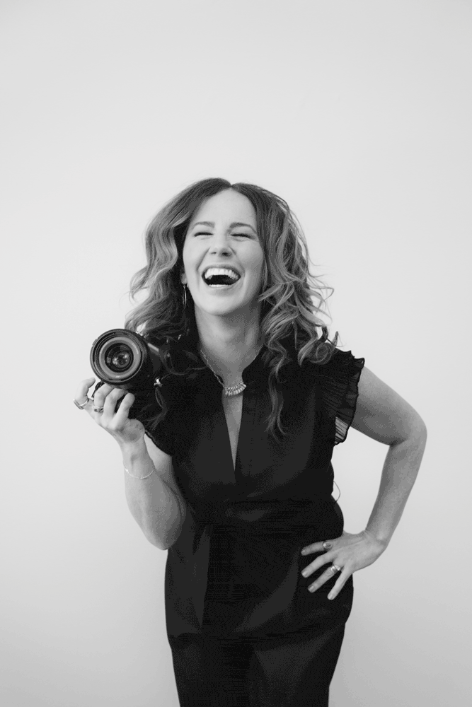 Woman laughing, holding camera, black and white portrait.