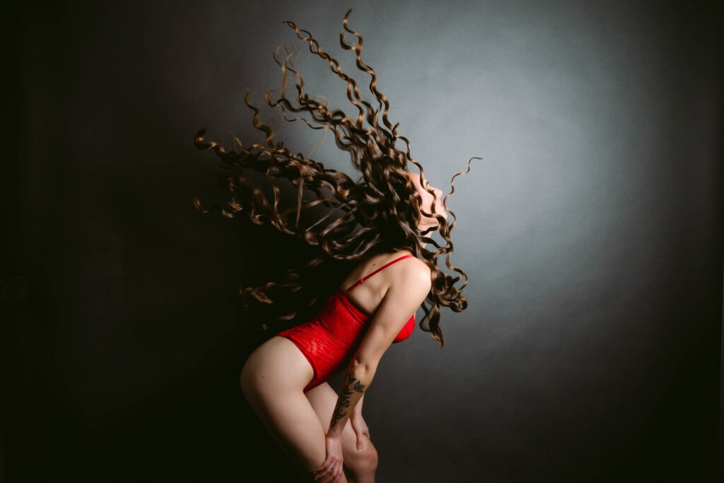 Woman in red bodysuit flipping curly hair.