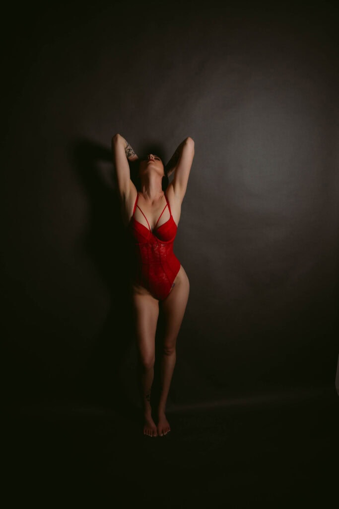 Woman in red lingerie poses against dark background.